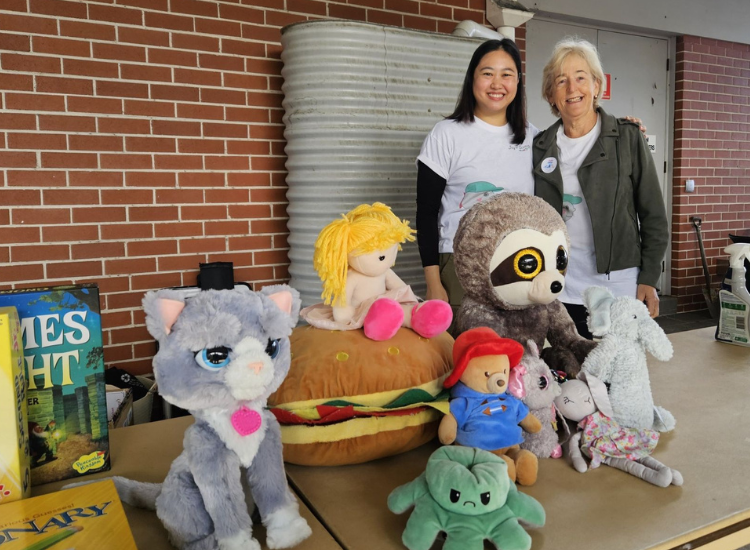 Two women smiling at the camera, standing behind a table full of stuffed animals.