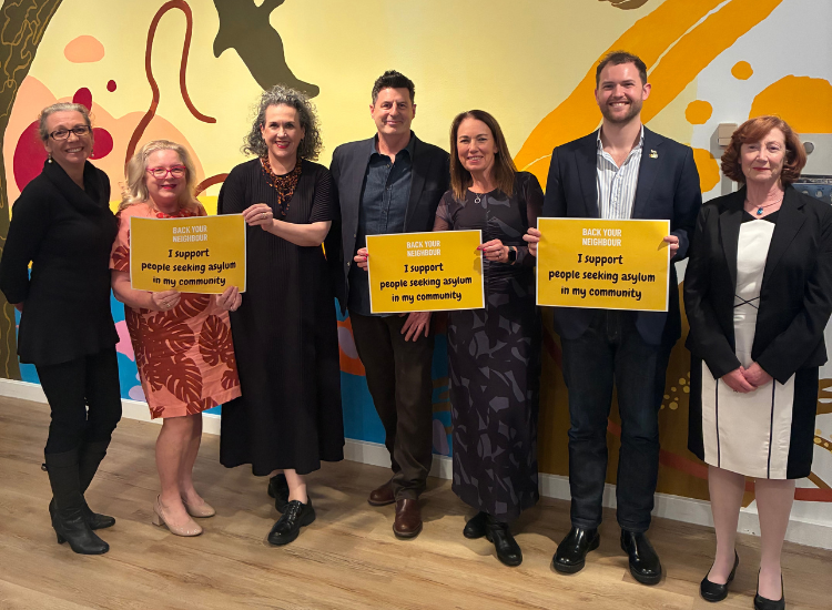 Seven North Sydney Councillors posing for a photo holding pledge signs that read: Back Your Neighbour - I support people seeking asylum in my community