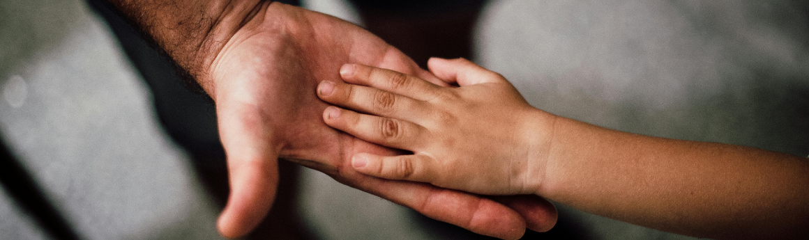 A close up shot of two hands - an outstretched adult hand, palm up, with a small child's hand on top of it