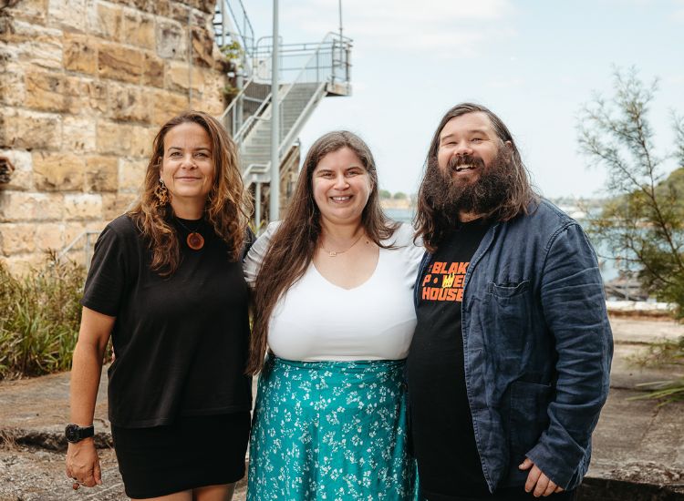 Three First Nations Australians standing together in front of a sandstone structure