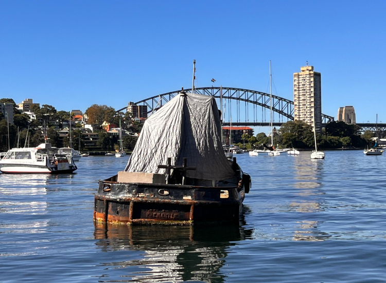 A dilapidated boat on the water in Berrys Bay, with the Sydney Harbour Bridge in the background