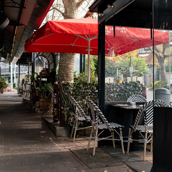 Outdoor dining tables and chairs set up beside a footpath, under umbrellas and awnings