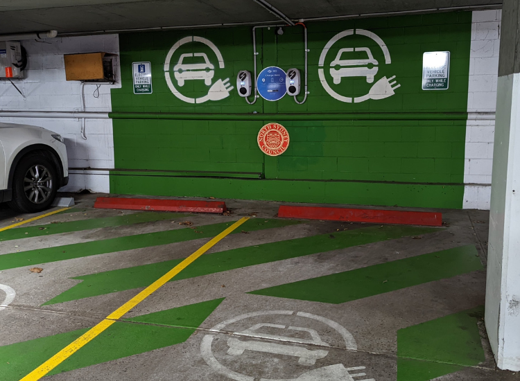 Two electric vehicle charging points installed on the wall of a car park. The wall is painted green and has the North Sydney Council logo.