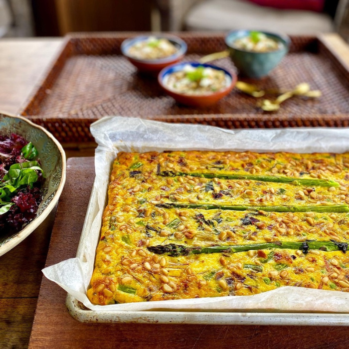 Food laid out on a table, including an asparagus and pine nut frittata in the foreground