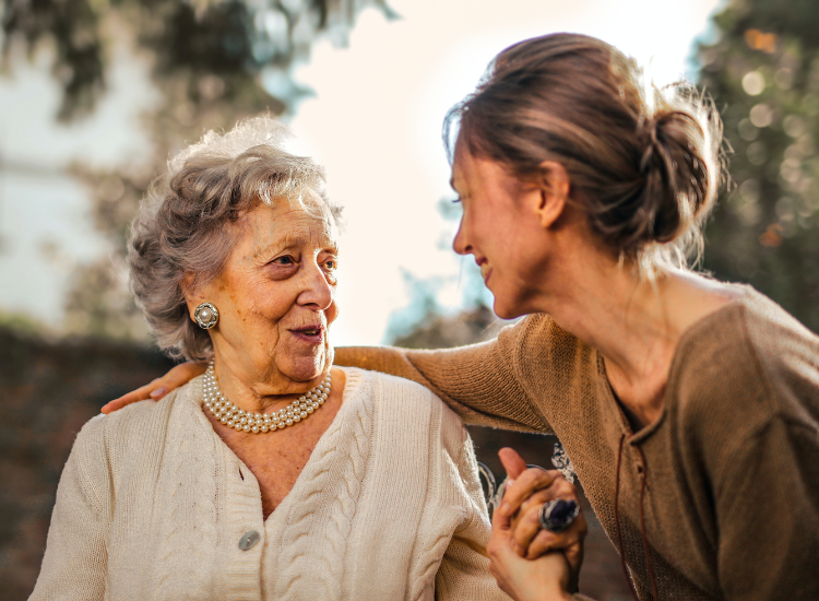 Photo of an elderly woman holding the hand of a younger woman.