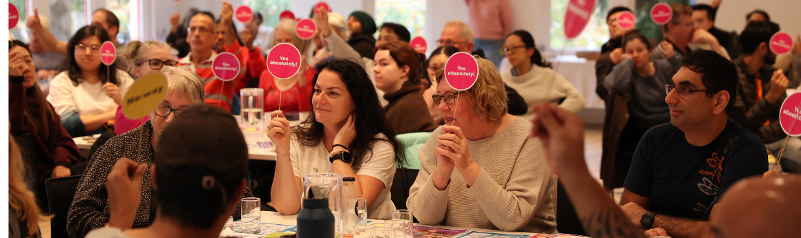 A group of people seated around tables in a hall holding small signs that read 'yes absolutely'