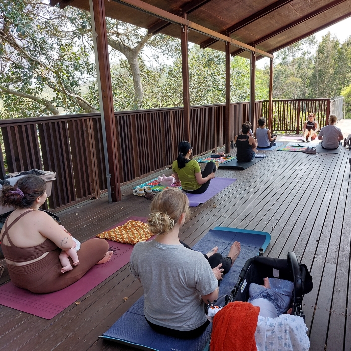 Mothers seated with their babies facing a yoga instructor