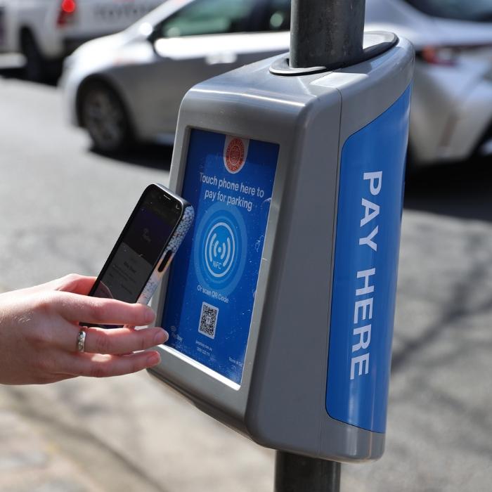 Grey box device attached to street poles to pay for parking with a blue sign on the side that says 'pay here'